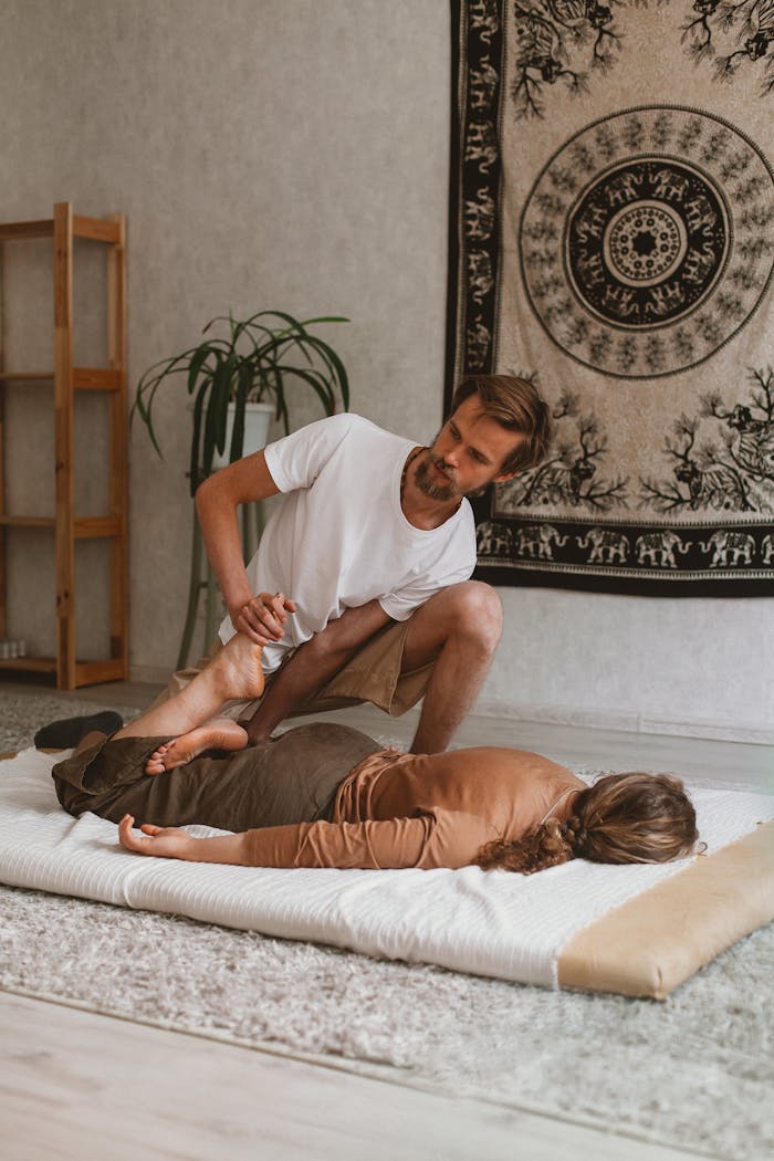 A man provides massage therapy to a woman on a mat in a peaceful indoor setting.